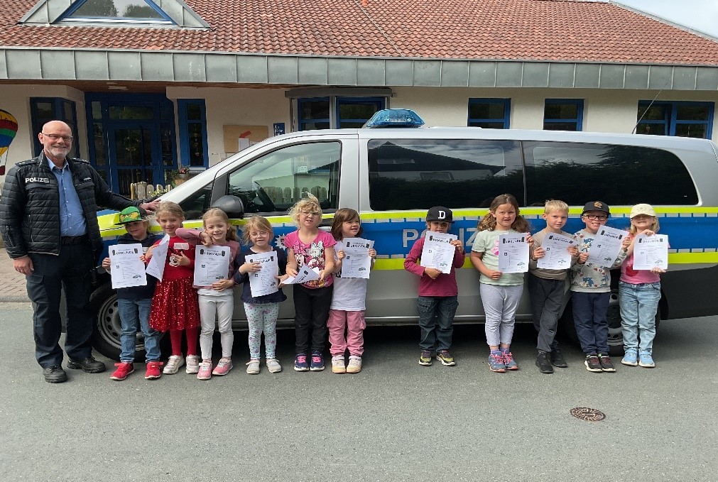 Schulanfänger mit Polizist vor einem Polizeiwagen