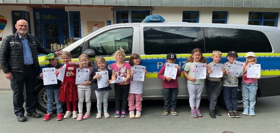 Schulanfänger mit Polizist vor einem Polizeiwagen